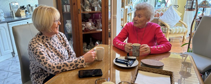 Elderly woman sitting at the dining room table with her daughter talking and drinking tea